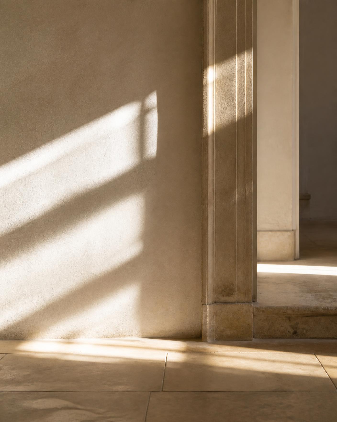 Daylight moving across a plaster wall and stone threshold